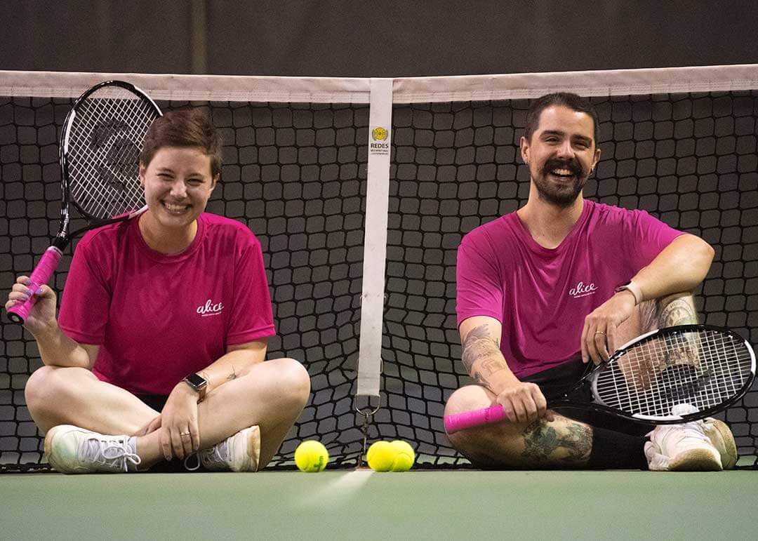 Mirella e Pedro sentados em uma quadra de tênis, segurando raquetes